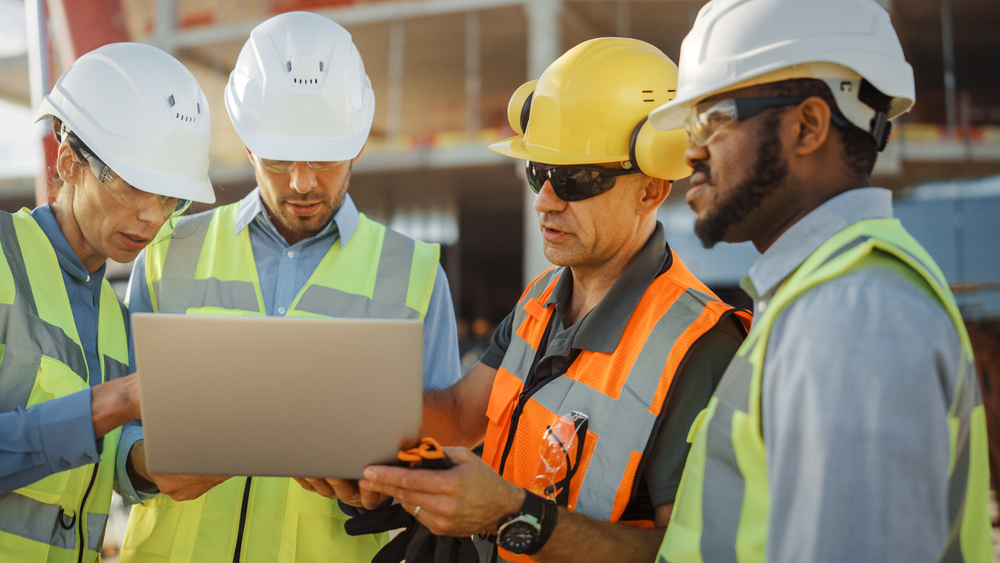 647888ca92d03e3fca3f239d Diverse Team of Specialists Use Laptop Computer on Construction Site